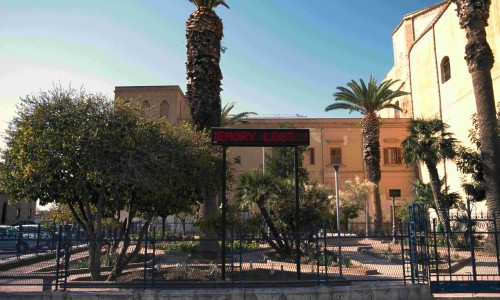 Public square with multiple palm trees, other trees, and a digital sign displaying red text 'EMORY LOST'.