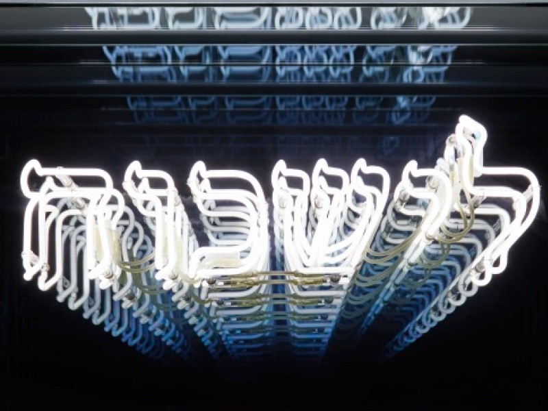 Leuchtendes, dreidimensionales Kunstwerk mit hebräischen Buchstaben in einem schwarzen Rahmen.