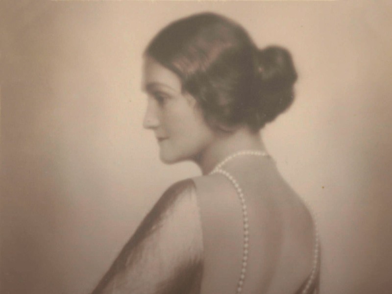 Porträt einer Frau mit hochgestecktem Haar und Perlenkette, Rückenansicht, sepiafarben.