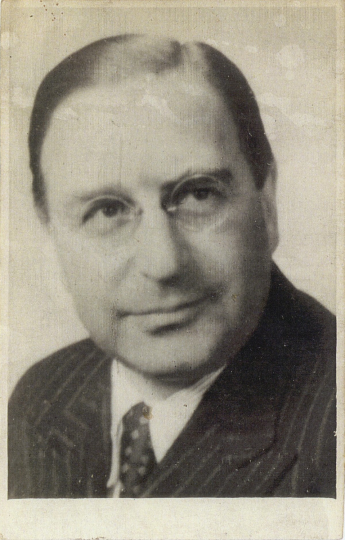: Man wearing a dark pinstripe suit, white shirt, and patterned tie in a vintage black and white portrait