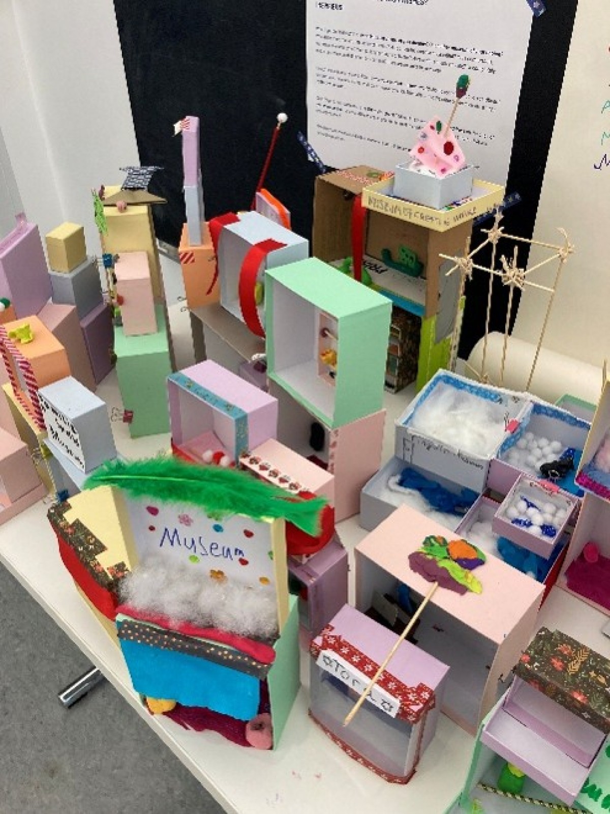 : Mehrere bunte, selbstgebastelte Modelle aus Pappe und Papier stehen auf einem Tisch, darunter ein Modell mit der Aufschrift 'Museum'.