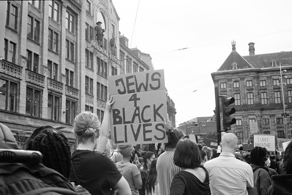 : Menschenmenge bei einer Demonstration in einer Stadt, eine Person hält ein Schild mit der Aufschrift 'JEWS 4 BLACK LIVES'