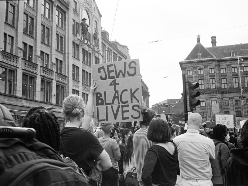 Menschenmenge bei einer Demonstration in einer Stadt, eine Person hält ein Schild mit der Aufschrift 'JEWS 4 BLACK LIVES'