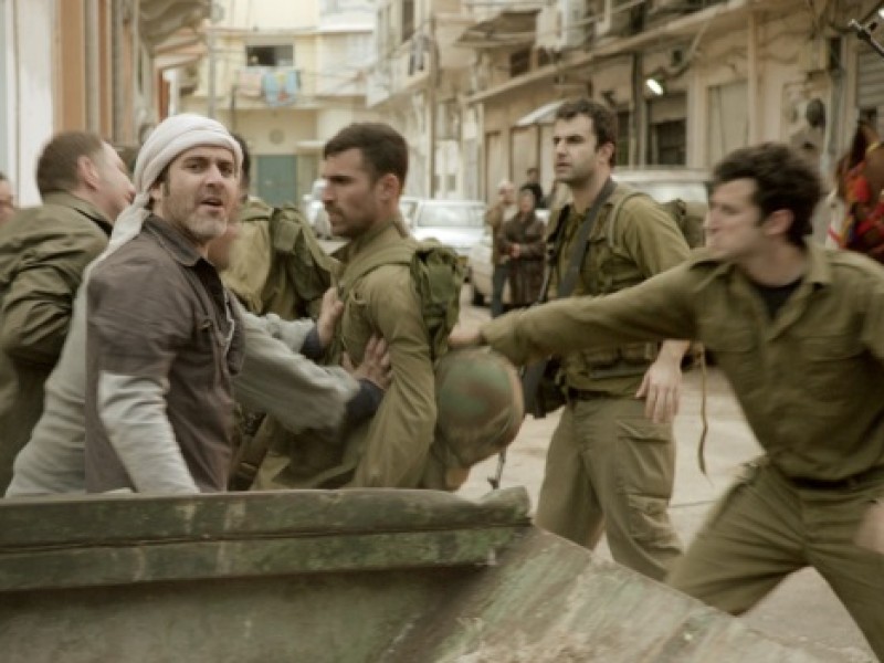 Group of men in an urban alley engaged in a tense confrontation, some wearing military uniforms and helmets.