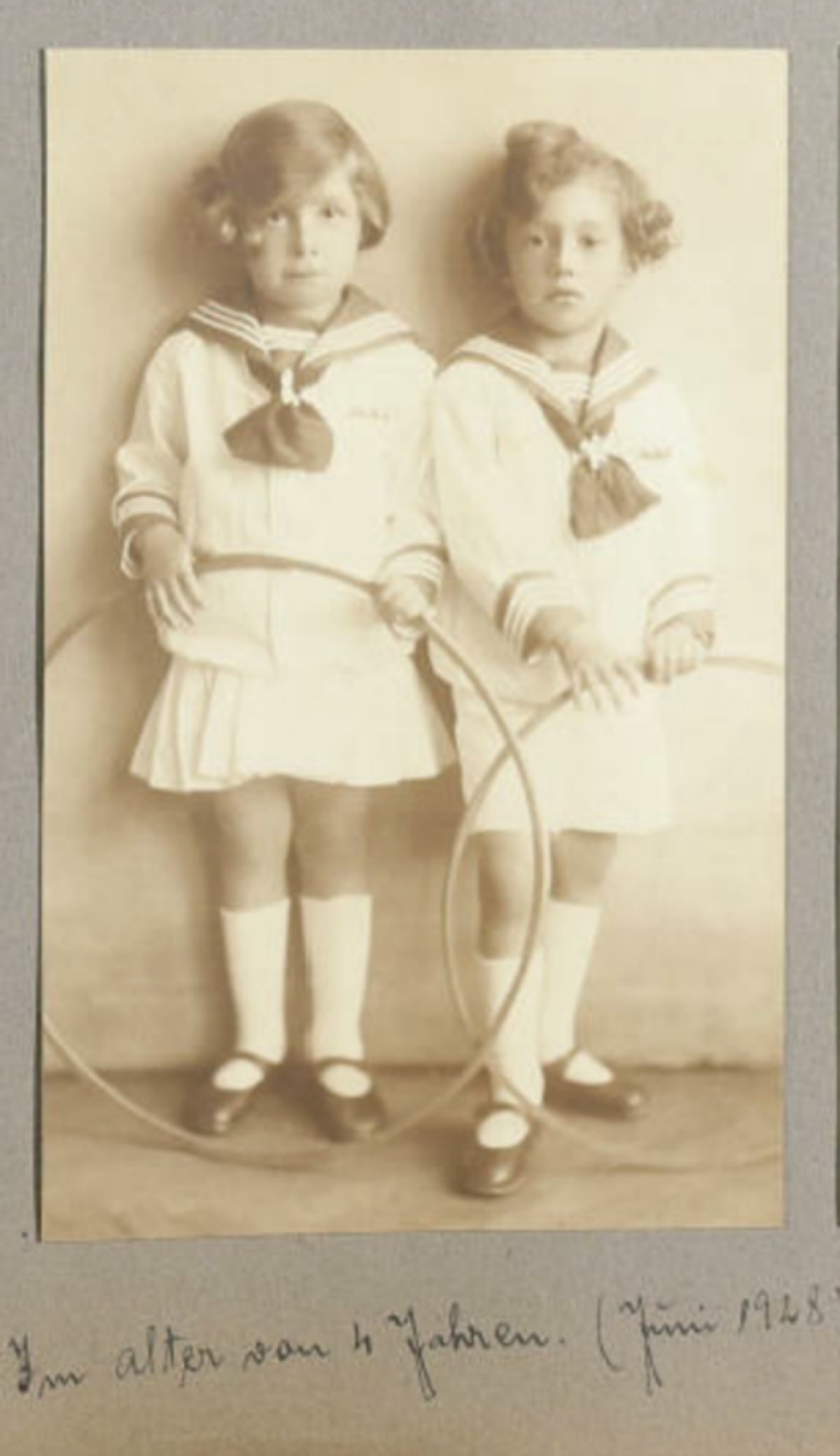 : Two young children in sailor-style outfits holding hoops, standing side by side