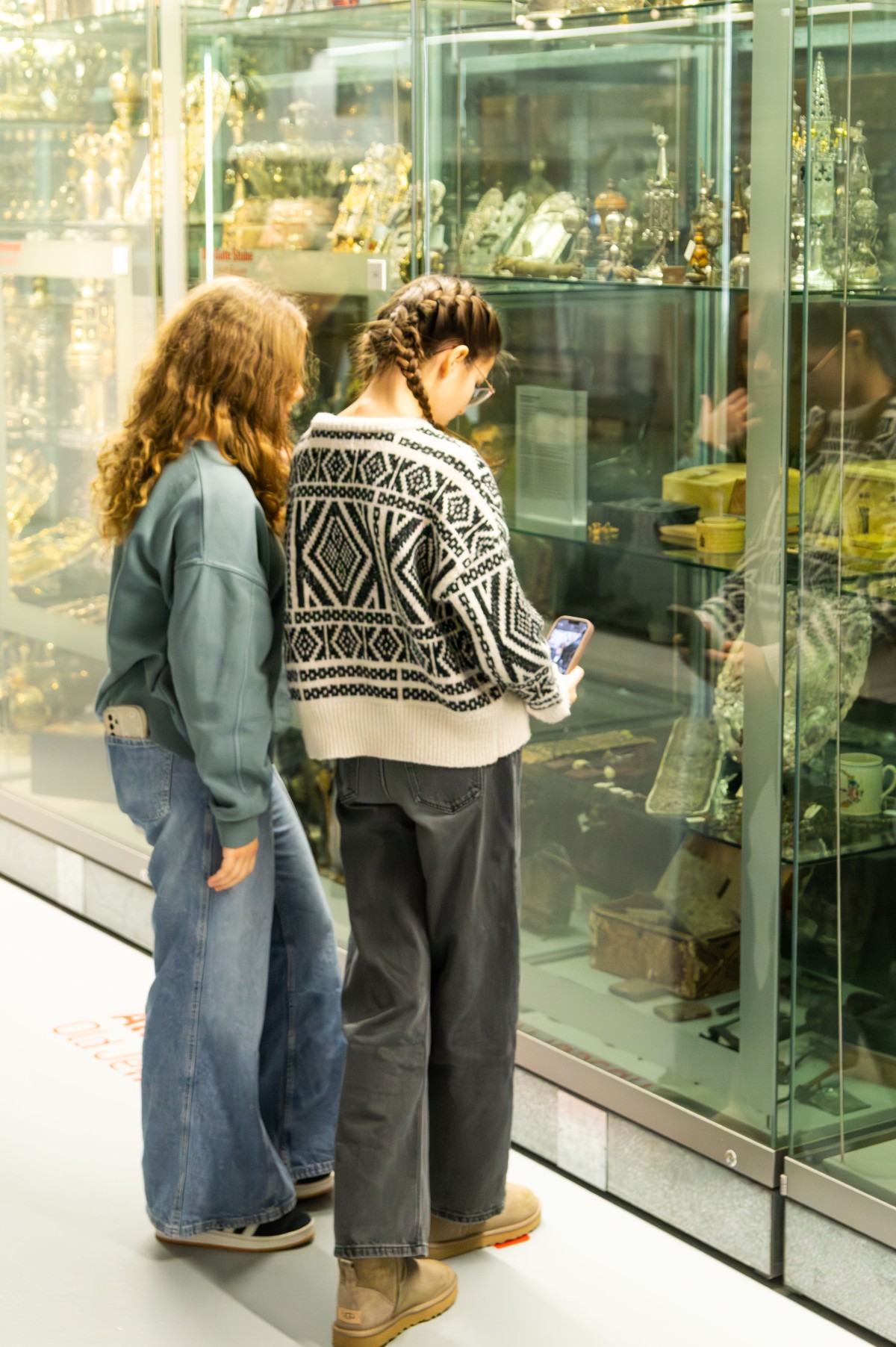 Jugendliche vor Museumsvitrine: Zwei Jugendliche vor einer Vitrine mit historischen jüdischen Artefakten im Museum, eine nutzt ein Smartphone.