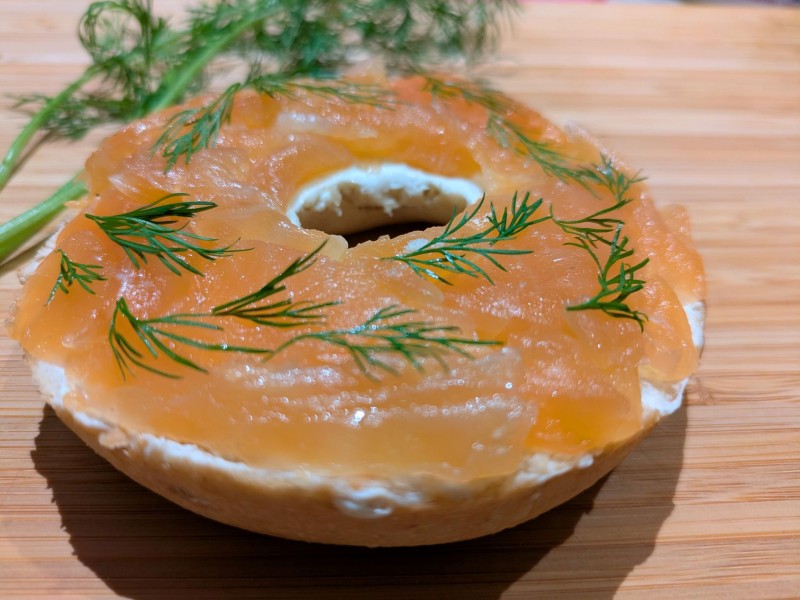 Bagel mit Frischkäse, Räucherlachs und Dill auf Holzuntergrund