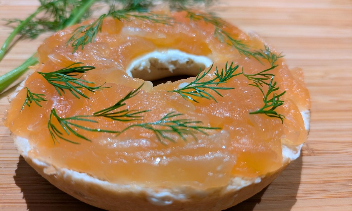 Bagel mit Frischkäse, Räucherlachs und Dill auf Holzuntergrund