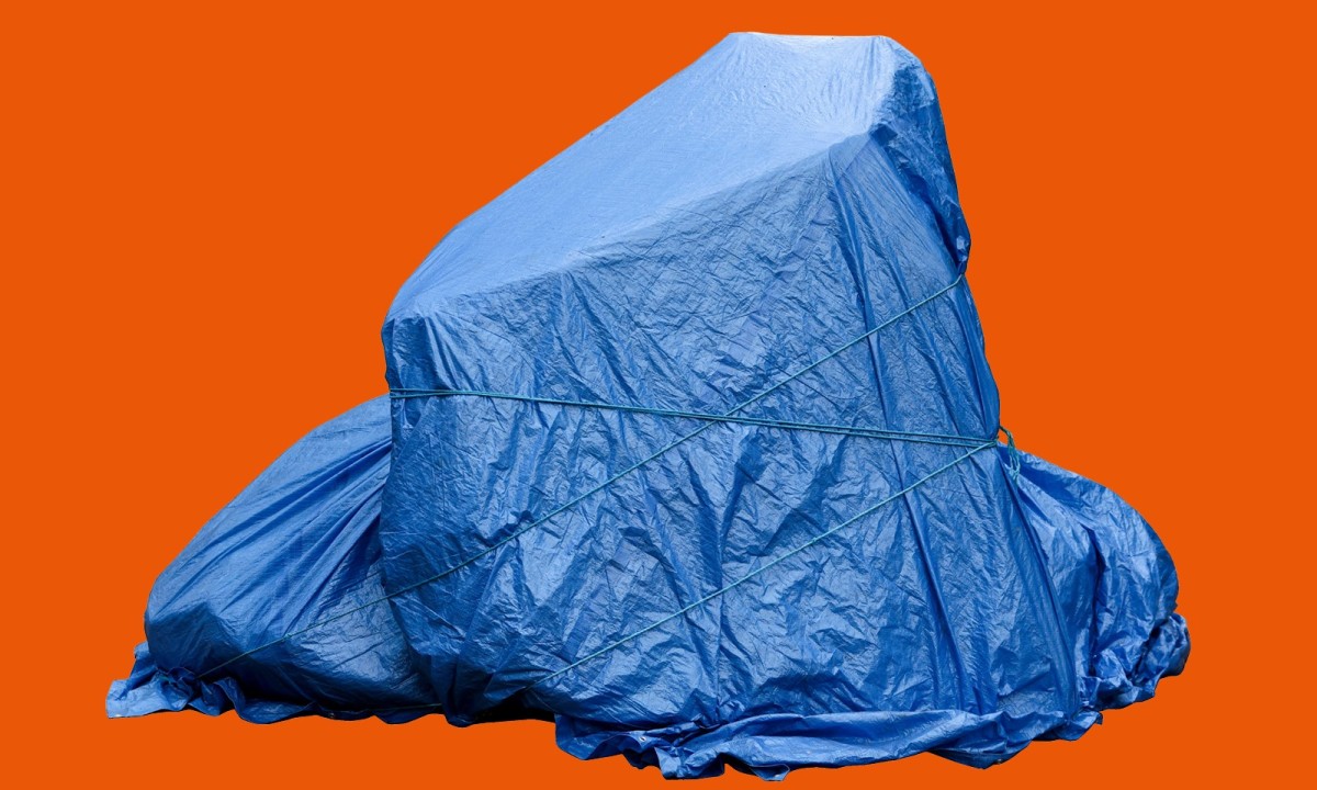 Großer Gegenstand mit blauer Plane abgedeckt und mit Seilen gesichert vor orangefarbenem Hintergrund