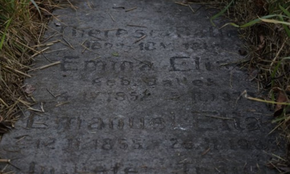 Grabstein mit verwitterter Inschrift und Gras an den Rändern