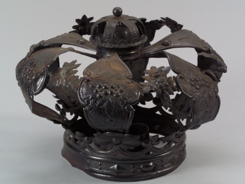 Metallkrone mit floralen Verzierungen und breiten, gebogenen Segmenten, die nach oben geöffnet sind.