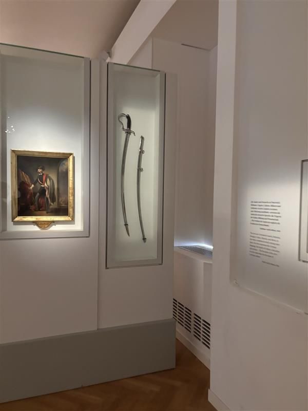 Historische Säbel und Porträt im Museum: Museumsausstellung mit zwei historischen Säbeln in einer Glasvitrine und einem Porträt eines Mannes in militärischer Kleidung im goldenen Rahmen