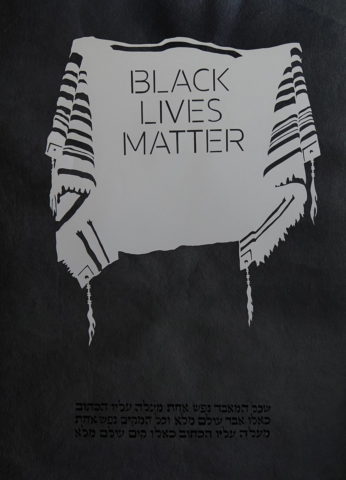 Tallit mit 'BLACK LIVES MATTER'-Text: Ein weißer Tallit mit schwarzen Streifen, darauf steht 'BLACK LIVES MATTER'. Darunter hebräischer Text in schwarzer Schrift.