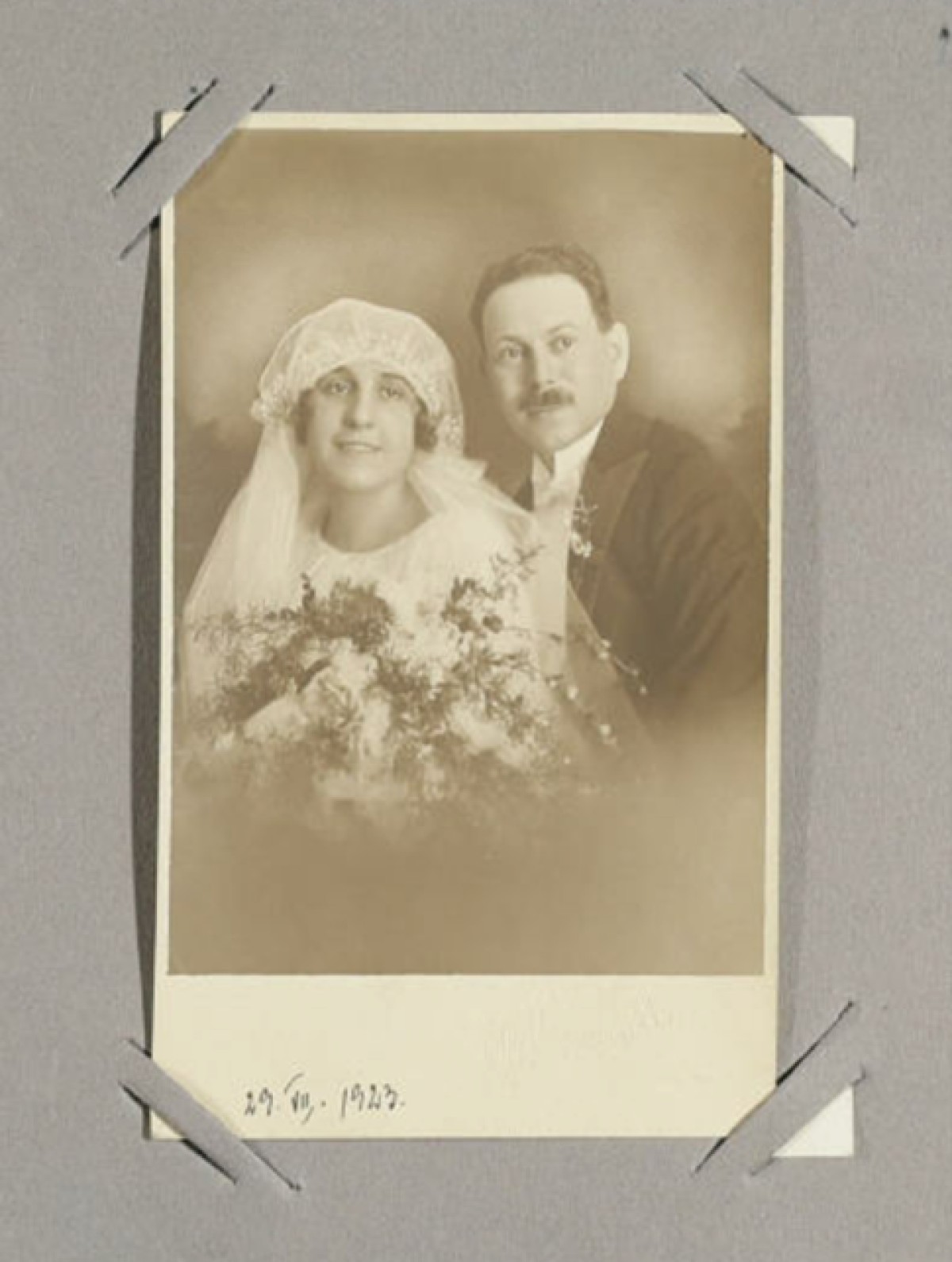 : Sepia-toned vintage wedding portrait of a bride in a veil and a groom in a suit, dated 29.VII.1923.