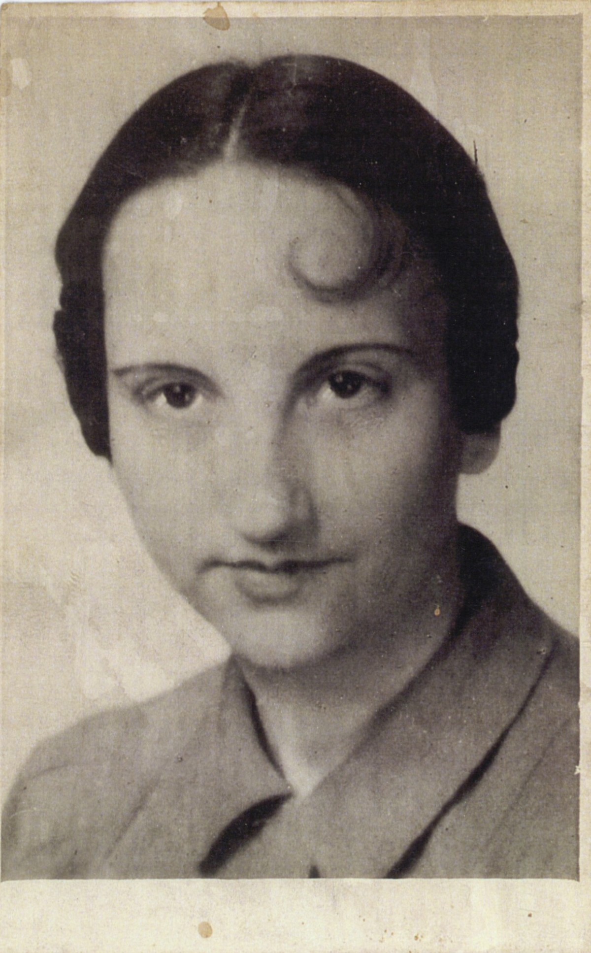 : Woman with dark hair styled in a 1920s or 1930s fashion, wearing a collared coat or jacket